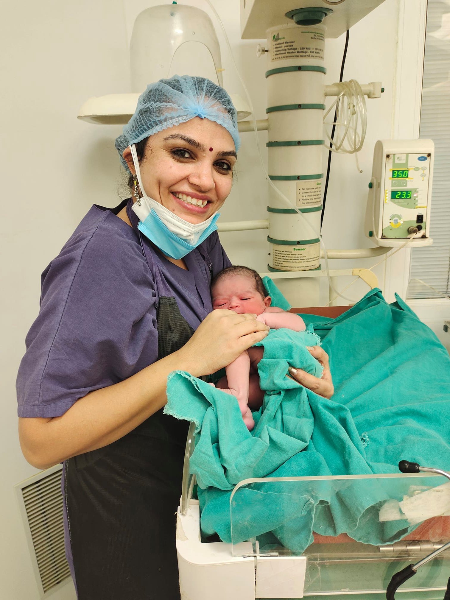 Smiling female doctor holding newborn baby in delivery room