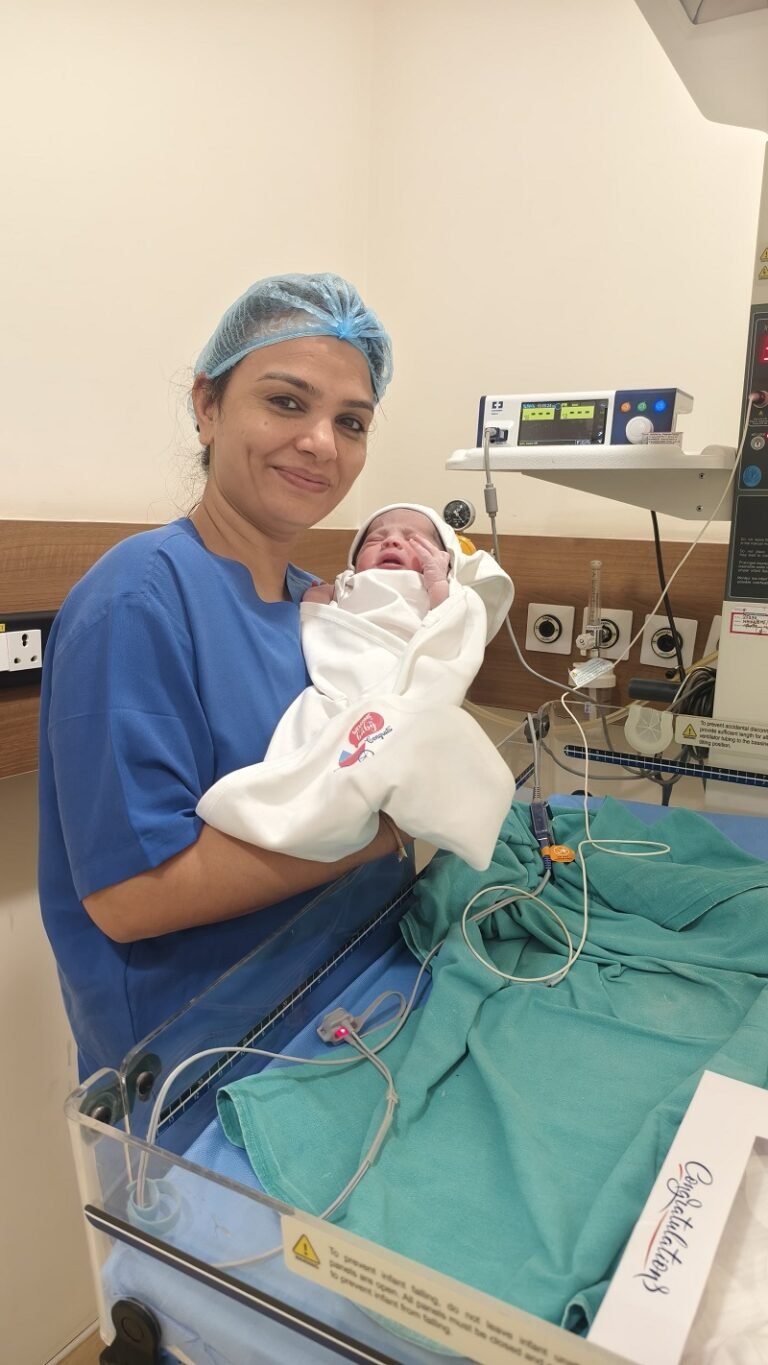 Dr. Archana Mohana, Best Lady Gynecologist in Indore, holding a newborn baby after a successful delivery in a hospital setting.