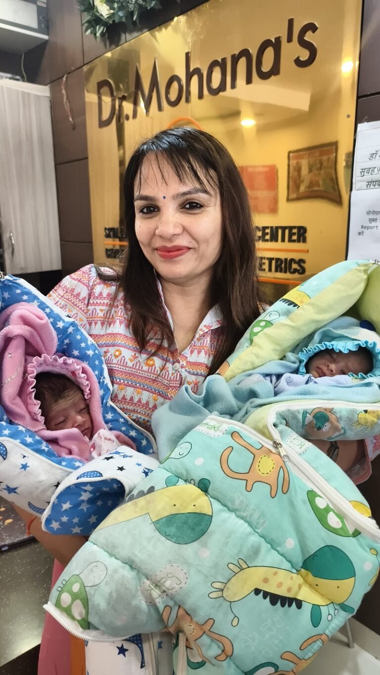 Dr. Archana Mohana smiling while holding twin newborns in colorful baby wraps at Dr. Mohana’s Skin & Gynae Centre.
