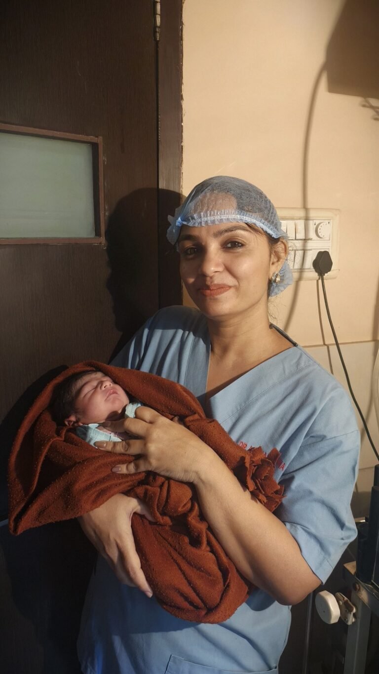 A smiling female doctor in scrubs holding a newborn baby wrapped in a brown blanket after delivery.