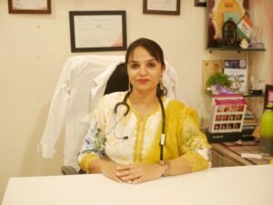 A gynecologist in a yellow floral outfit with a stethoscope around her neck, seated at her clinic desk, ready for patient consultation.